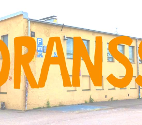 Oranssin logo suvilahden keltaisen rakennuksen päällä